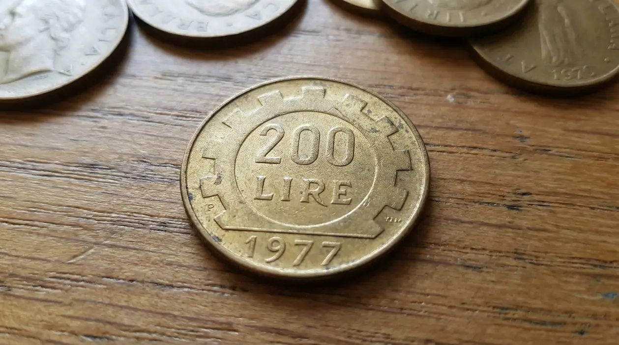 Primo piano di una moneta da 200 lire del 1977 su un tavolo di legno, con altre monete sullo sfondo