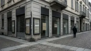 Vetrine di negozi chiusi in centro città con serrande abbassate e una persona che cammina sul marciapiede