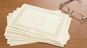 Certificati cartacei impilati su un tavolo in legno con occhiali da vista accanto