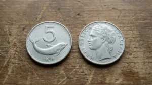 Due monete italiane da 5 lire con delfino, viste su entrambi i lati, appoggiate su un tavolo di legno