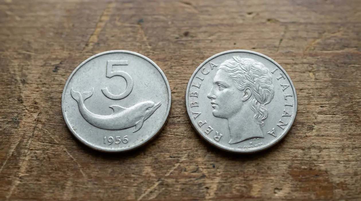 Due monete italiane da 5 lire con delfino, viste su entrambi i lati, appoggiate su un tavolo di legno