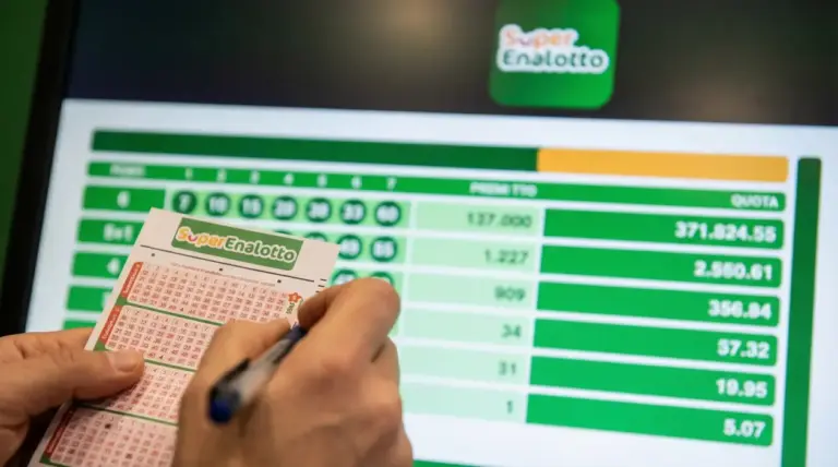 Mani che compilano una schedina del SuperEnalotto davanti a uno schermo con risultati e quote di vincita